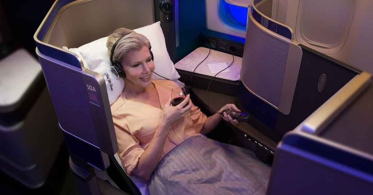 a women in a united Polaris business class half lie down with a wine glass in her hand and using headphone